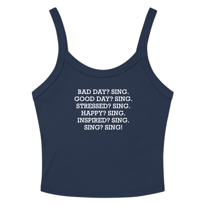 "Bad Day? Sing. Good Day? Sing. Stressed? Sing. Happy? Sing. Inspired? Sing. Sing? Sing!" printed on a solid navy blend women's micro-rib tanktop laying on a flat surface amongst sunglasses and shorts