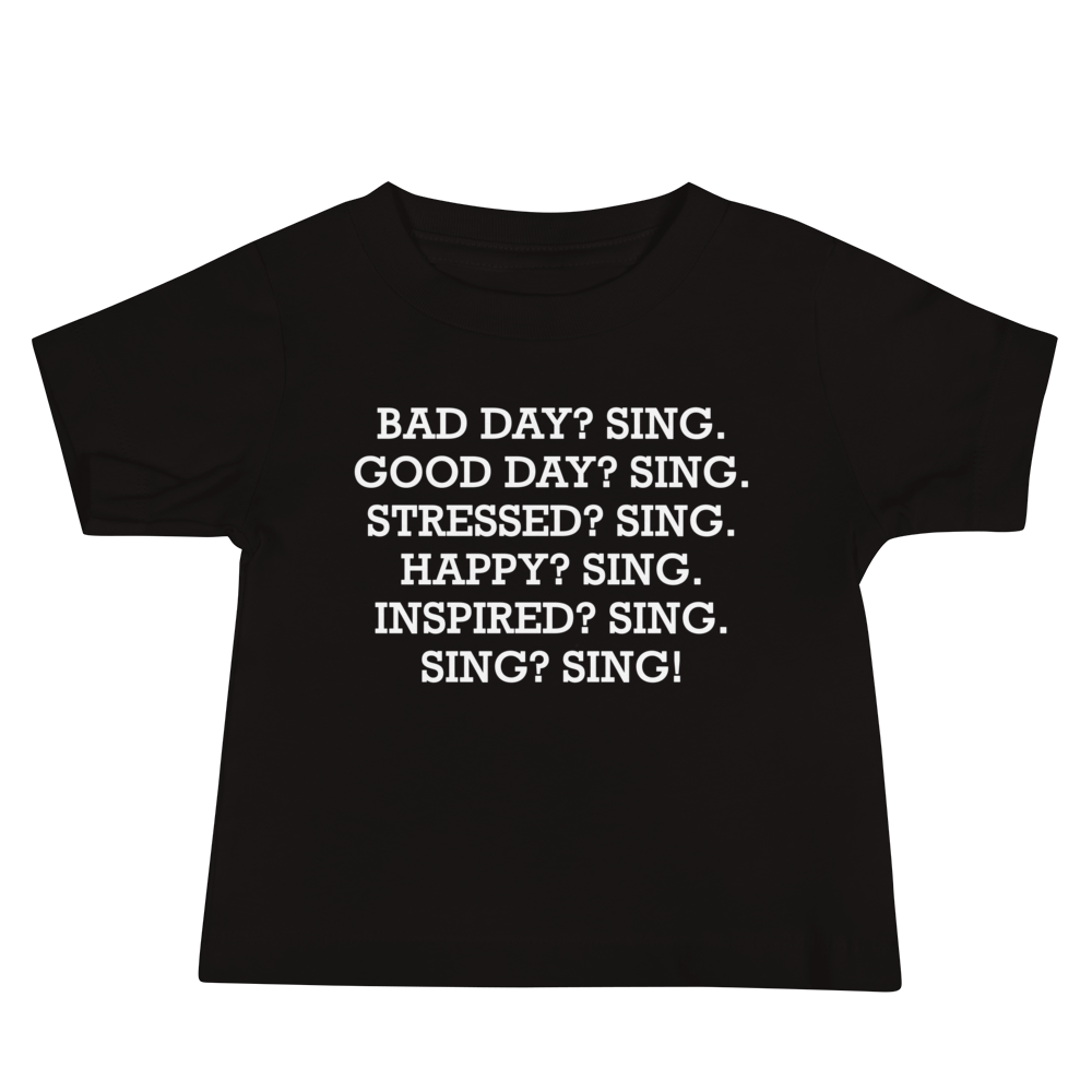 "Bad Day? Sing. Good Day? Sing. Stressed? Sing. Happy? Sing. Inspired? Sing. Sing? Sing!" printed on a black baby jersey short sleeve tee laying on a flat surface
