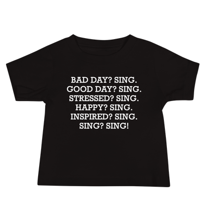 "Bad Day? Sing. Good Day? Sing. Stressed? Sing. Happy? Sing. Inspired? Sing. Sing? Sing!" printed on a black baby jersey short sleeve tee laying on a flat surface