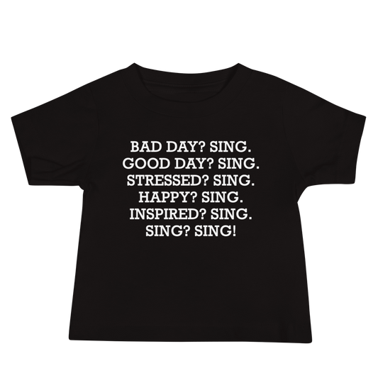 "Bad Day? Sing. Good Day? Sing. Stressed? Sing. Happy? Sing. Inspired? Sing. Sing? Sing!" printed on a black baby jersey short sleeve tee laying on a flat surface