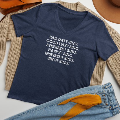 "Bad Day? Sing. Good Day? Sing. Stressed? Sing. Happy? Sing. Inspired? Sing. Sing? Sing!" printed on a heather navy women's relaxed v-neck t-shirt laying on a flat surface amongst other clothes