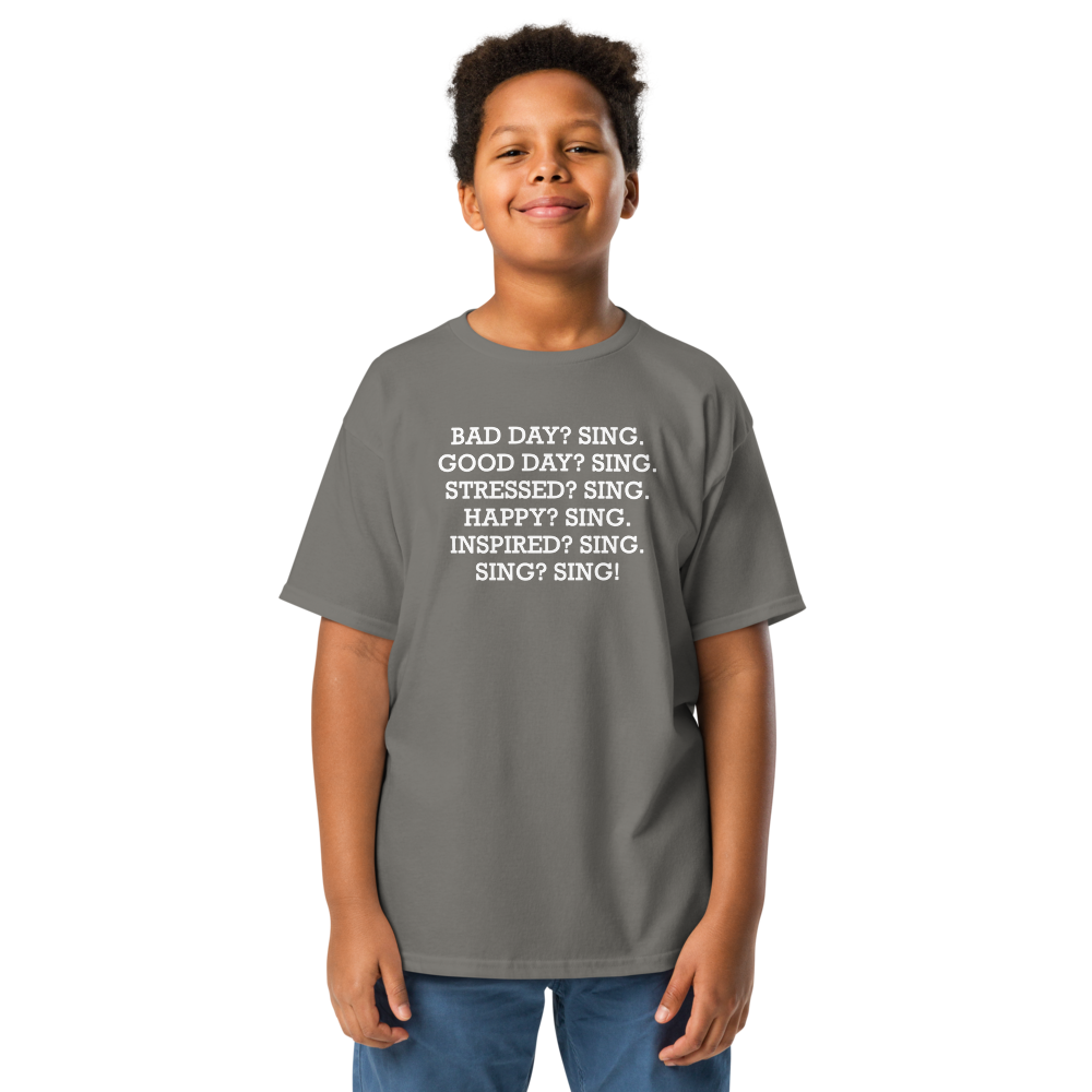 "Bad Day? Sing. Good Day? Sing. Stressed? Sing. Happy? Sing. Inspired? Sing. Sing? Sing!" printed on a charcoal youth classic tee worn by a male