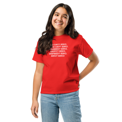 "Bad Day? Sing. Good Day? Sing. Stressed? Sing. Happy? Sing. Inspired? Sing. Sing? Sing!" printed on a red youth classic tee worn by a female