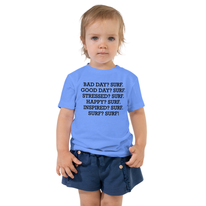 "Bad Day? Surf. Good Day? Surf. Stressed? Surf. Happy? Surf. Inspired? Surf. Surf? Surf!" printed on a heather columbia blue toddler short sleeve tee worn by a female