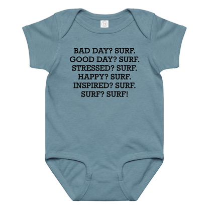"Bad Day? Surf. Good Day? Surf. Stressed? Surf. Happy? Surf. Inspired? Surf. Surf? Surf!" printed on a vintage indigo baby jersey bodysuit laying on a flat surface amongst other clothes
