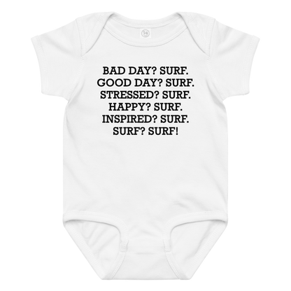 "Bad Day? Surf. Good Day? Surf. Stressed? Surf. Happy? Surf. Inspired? Surf. Surf? Surf!" printed on a white baby jersey bodysuit laying on a flat surface amongst other clothes