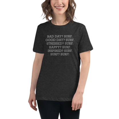 "Bad Day? Surf. Good Day? Surf. Stressed? Surf. Happy? Surf. Inspired? Surf. Surf? Surf!" printed on a dark grey heather women's relaxed t-shirt worn by a female