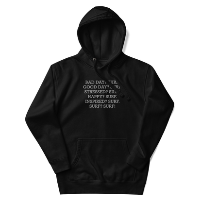 "Bad Day? Surf. Good Day? Surf. Stressed? Surf. Happy? Surf. Inspired? Surf. Surf? Surf!" printed on a black unisex hoodie laying on a flat surface with the hood up