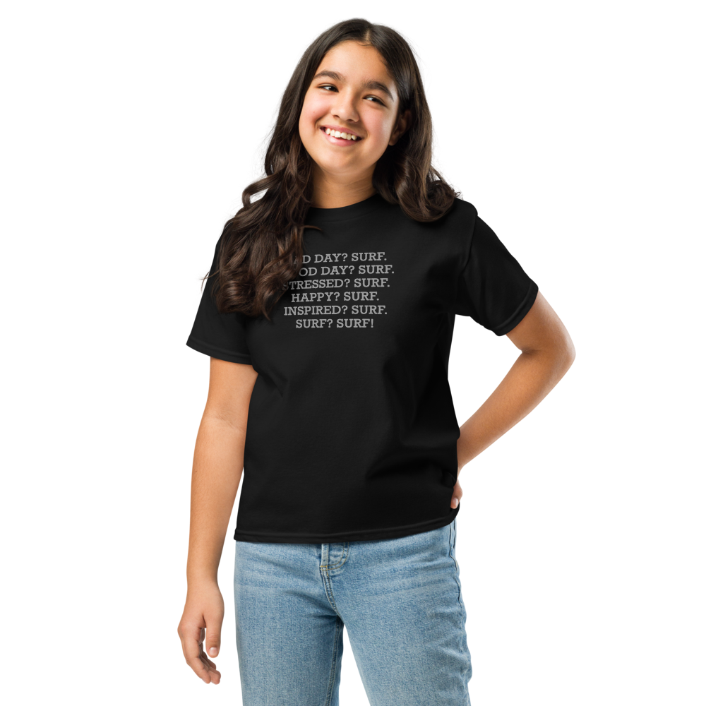 "Bad Day? Surf. Good Day? Surf. Stressed? Surf. Happy? Surf. Inspired? Surf. Surf? Surf!" printed on a black youth classic tee worn by a female