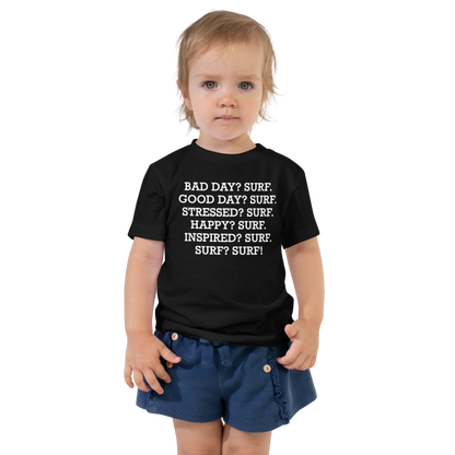 "Bad Day? Surf. Good Day? Surf. Stressed? Surf. Happy? Surf. Inspired? Surf. Surf? Surf!" printed on a black toddler short sleeve tee worn by a female