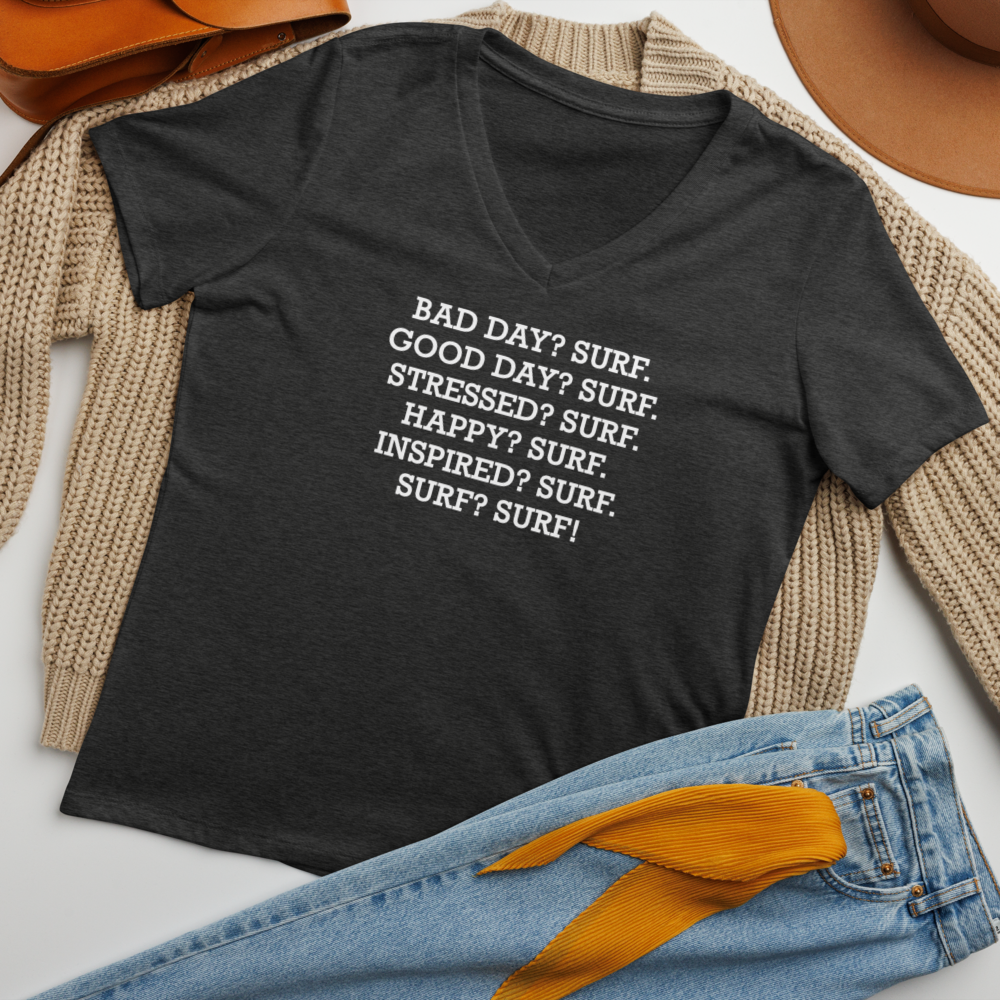 "Bad Day? Surf. Good Day? Surf. Stressed? Surf. Happy? Surf. Inspired? Surf. Surf? Surf!" printed on a dark grey heather women's relaxed v-neck t-shirt laying on a flat surface amongst other clothes