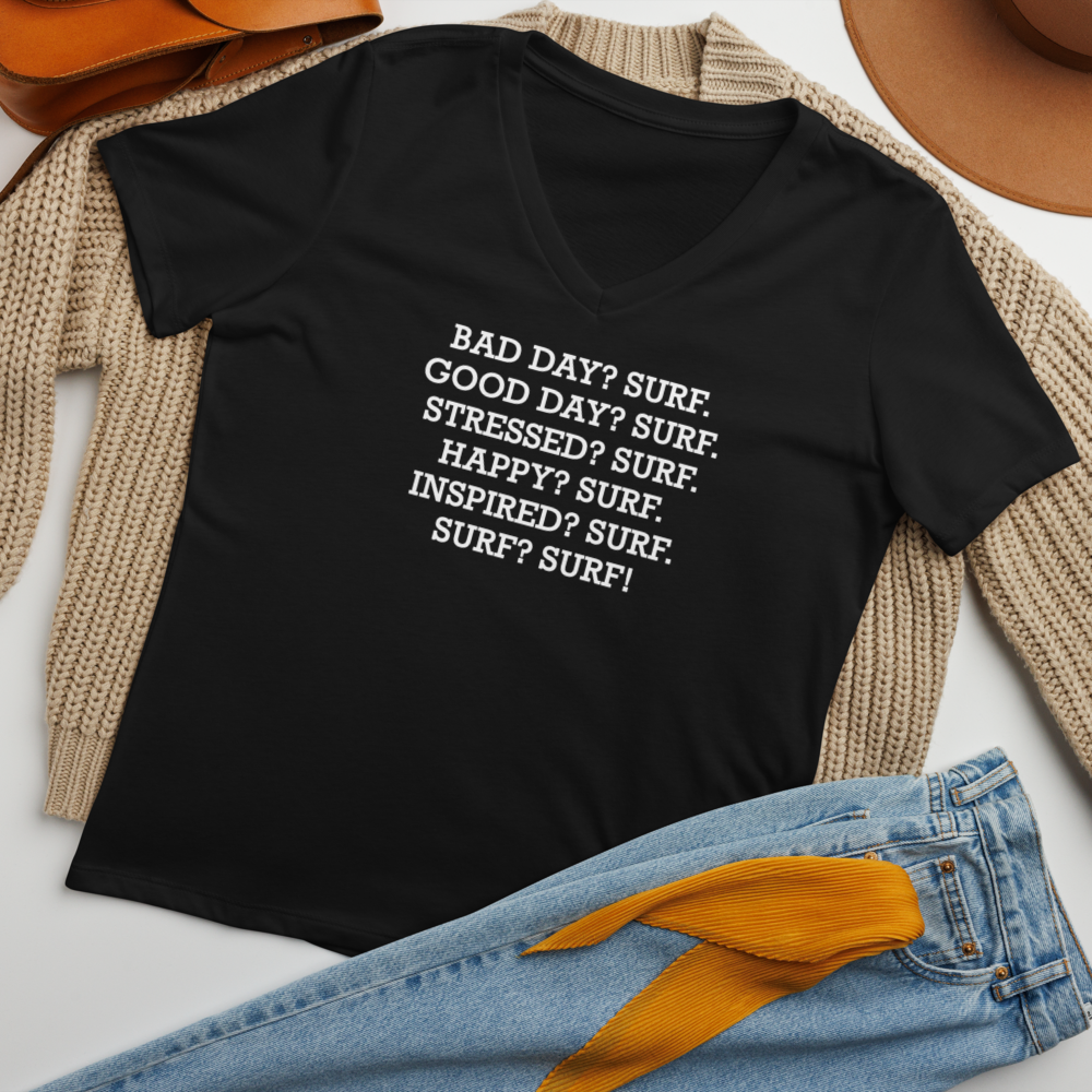 "Bad Day? Surf. Good Day? Surf. Stressed? Surf. Happy? Surf. Inspired? Surf. Surf? Surf!" printed on a solid black blend women's relaxed v-neck t-shirt laying on a flat surface amongst other clothes