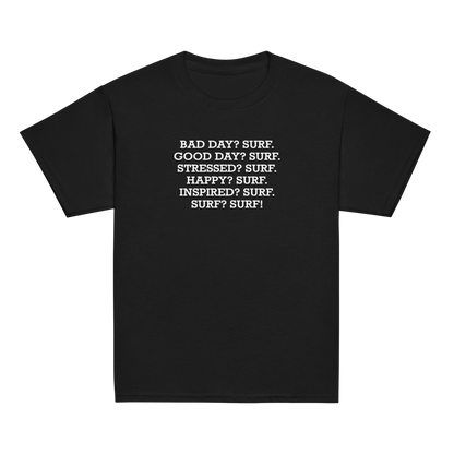 "Bad Day? Surf. Good Day? Surf. Stressed? Surf. Happy? Surf. Inspired? Surf. Surf? Surf!" printed on a black youth classic tee laying on a flat surface