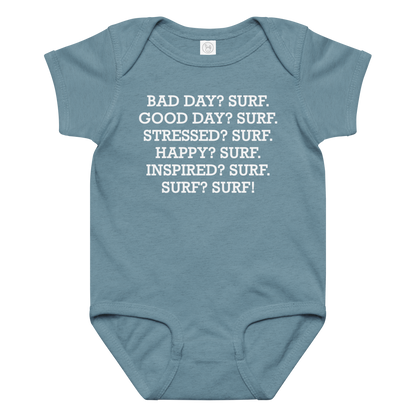 "Bad Day? Surf. Good Day? Surf. Stressed? Surf. Happy? Surf. Inspired? Surf. Surf? Surf!" printed on a vintage indigo baby jersey bodysuit laying on a flat surface amongst other clothes
