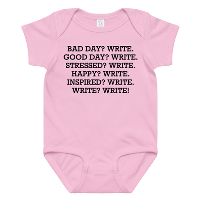 "Bad Day? Write. Good Day? Write. Stressed? Write. Happy? Write. Inspired? Write. Write? Write!" printed on a pink baby jersey bodysuit laying on a flat surface amongst other clothes