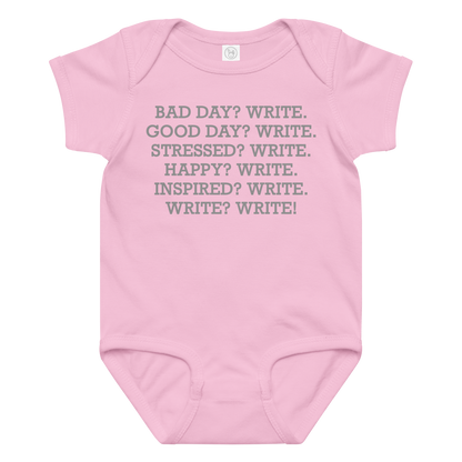 "Bad Day? Write. Good Day? Write. Stressed? Write. Happy? Write. Inspired? Write. Write? Write!" printed on a pink baby jersey bodysuit laying on a flat surface amongst other clothes