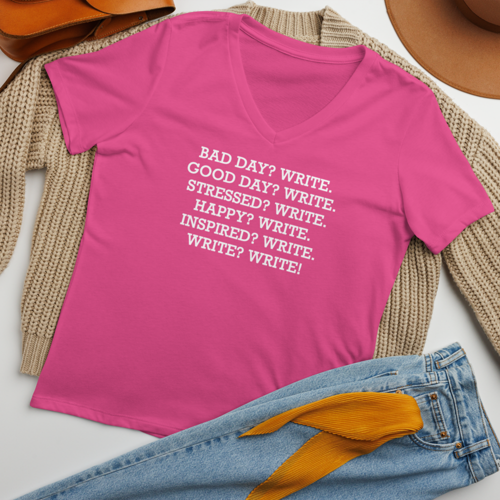 "Bad Day? Write. Good Day? Write. Stressed? Write. Happy? Write. Inspired? Write. Write? Write!" printed on a berry women's relaxed v-neck t-shirt laying on a flat surface amongst other clothes