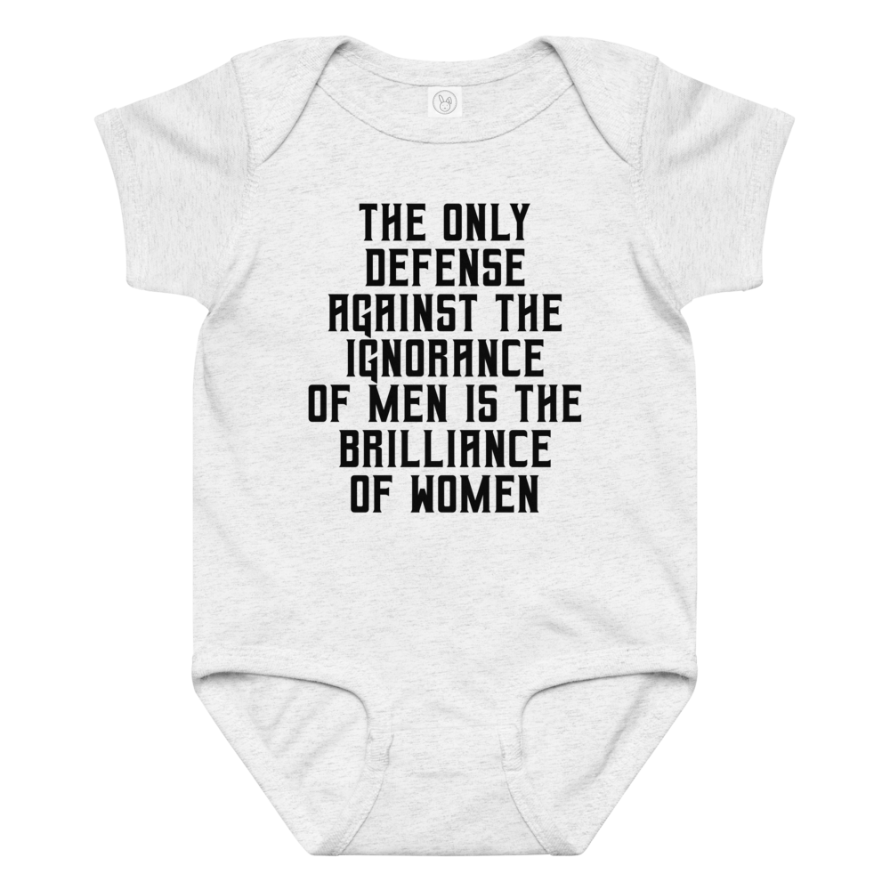 "The Only defense against the ignorance of men is the brilliance of women" printed on a ash baby jersey bodysuit laying on a flat surface amongst other clothes