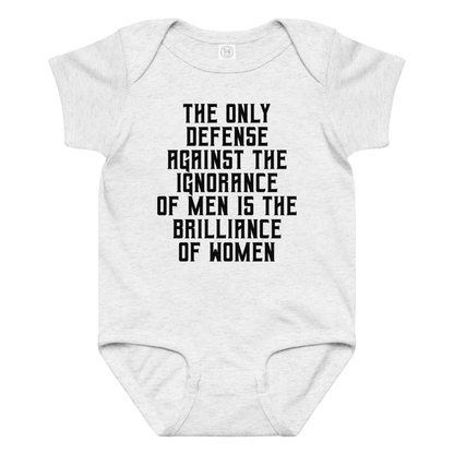 "The Only defense against the ignorance of men is the brilliance of women" printed on a ash baby jersey bodysuit laying on a flat surface amongst other clothes