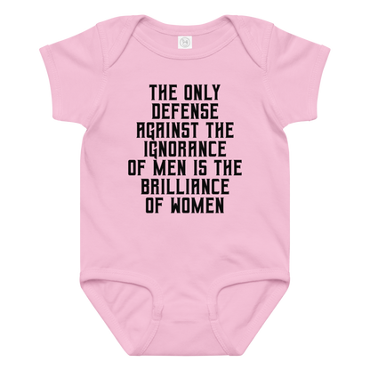 "The Only defense against the ignorance of men is the brilliance of women" printed on a pink baby jersey bodysuit laying on a flat surface amongst other clothes