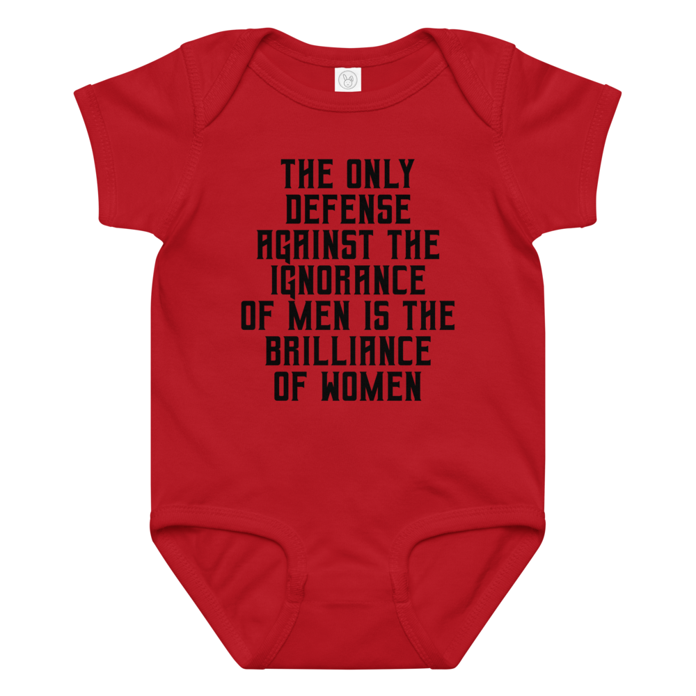 "The Only defense against the ignorance of men is the brilliance of women" printed on a red baby jersey bodysuit laying on a flat surface amongst other clothes