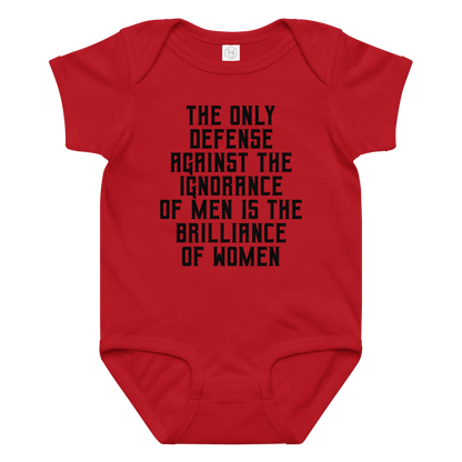 "The Only defense against the ignorance of men is the brilliance of women" printed on a red baby jersey bodysuit laying on a flat surface amongst other clothes