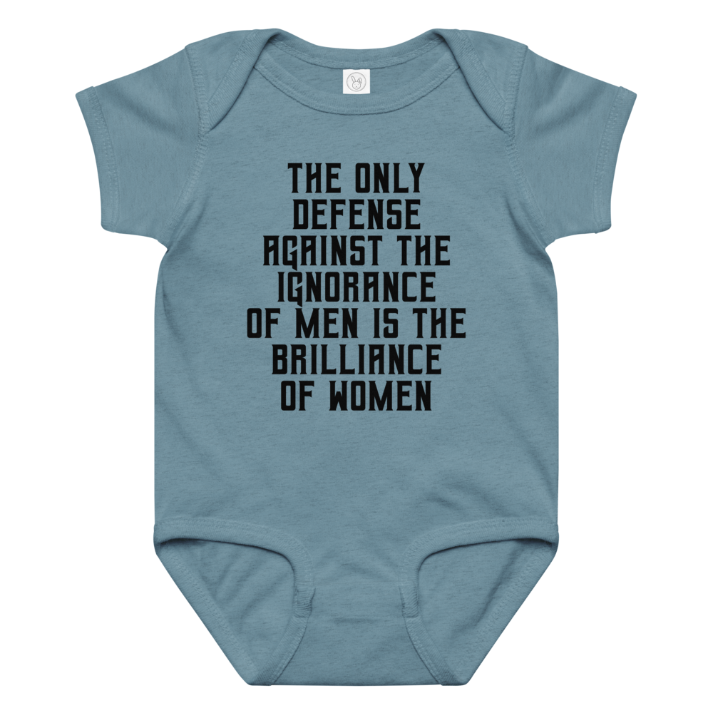 "The Only defense against the ignorance of men is the brilliance of women" printed on a vintage indigo baby jersey bodysuit laying on a flat surface amongst other clothes