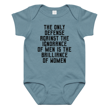 "The Only defense against the ignorance of men is the brilliance of women" printed on a vintage indigo baby jersey bodysuit laying on a flat surface amongst other clothes
