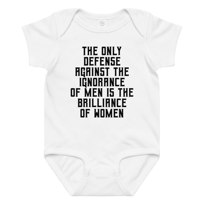 "The Only defense against the ignorance of men is the brilliance of women" printed on a white baby jersey bodysuit laying on a flat surface amongst other clothes