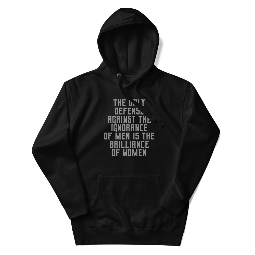 "The Only defense against the ignorance of men is the brilliance of women" printed on a black unisex hoodie laying on a flat surface with the hood up