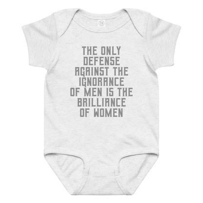 "The Only defense against the ignorance of men is the brilliance of women" printed on a ash baby jersey bodysuit laying on a flat surface amongst other clothes
