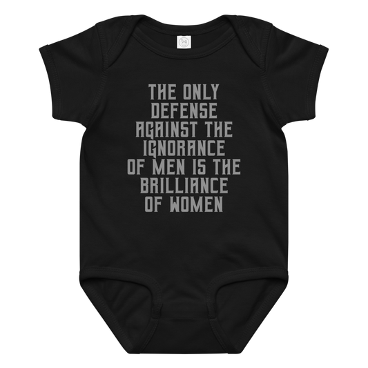"The Only defense against the ignorance of men is the brilliance of women" printed on a black baby jersey bodysuit laying on a flat surface amongst other clothes