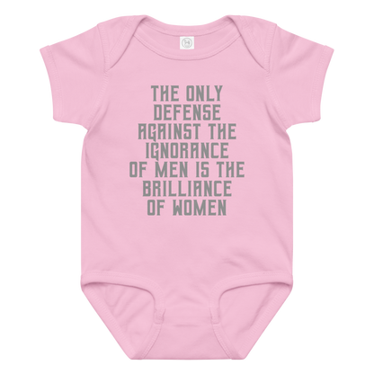 "The Only defense against the ignorance of men is the brilliance of women" printed on a pink baby jersey bodysuit laying on a flat surface amongst other clothes