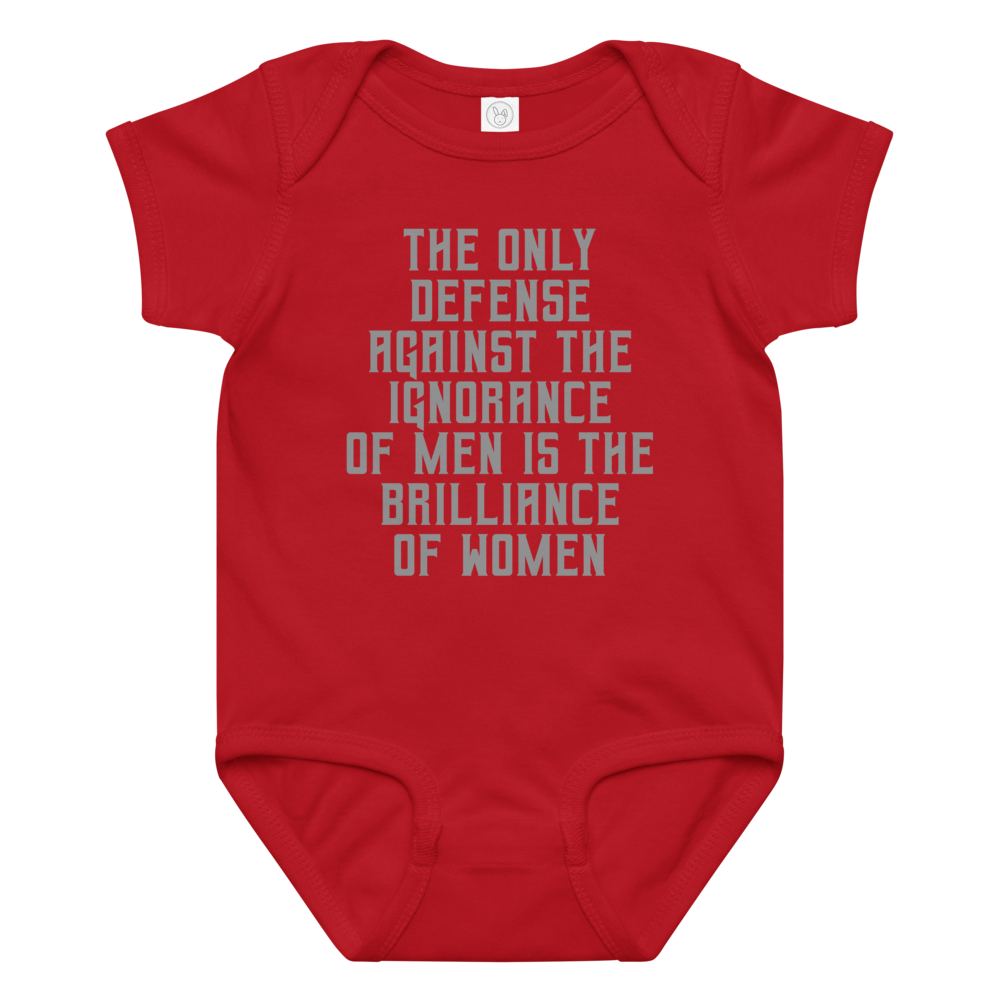 "The Only defense against the ignorance of men is the brilliance of women" printed on a red baby jersey bodysuit laying on a flat surface amongst other clothes