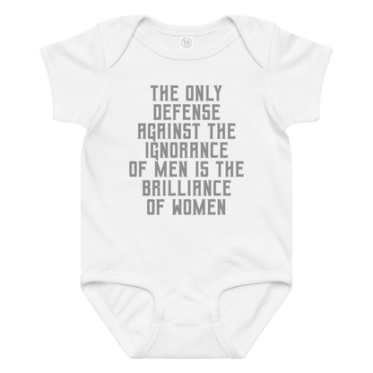 "The Only defense against the ignorance of men is the brilliance of women" printed on a white baby jersey bodysuit laying on a flat surface amongst other clothes