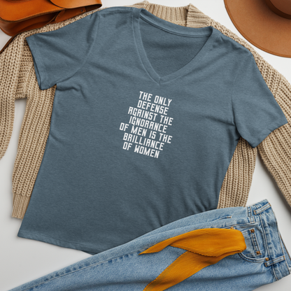 "The Only defense against the ignorance of men is the brilliance of women" printed on a heather slate women's relaxed v-neck t-shirt laying on a flat surface amongst other clothes