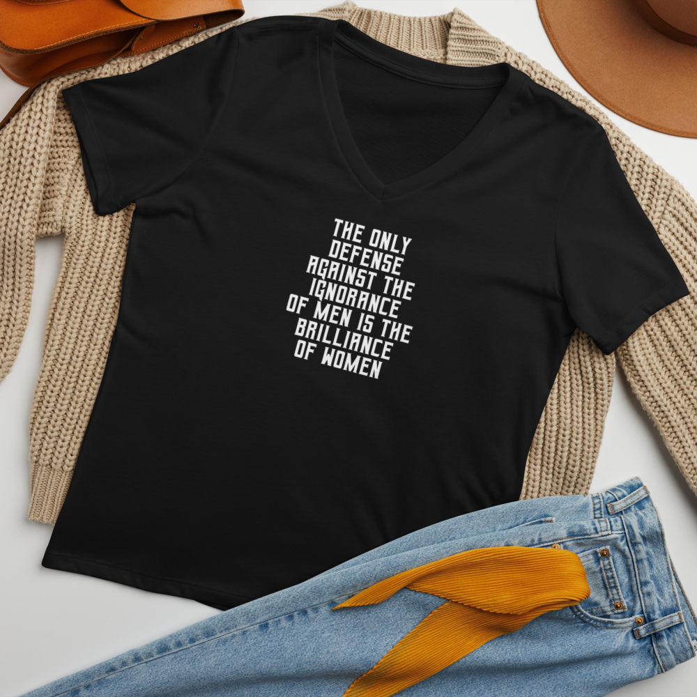 "The Only defense against the ignorance of men is the brilliance of women" printed on a solid black blend women's relaxed v-neck t-shirt laying on a flat surface amongst other clothes