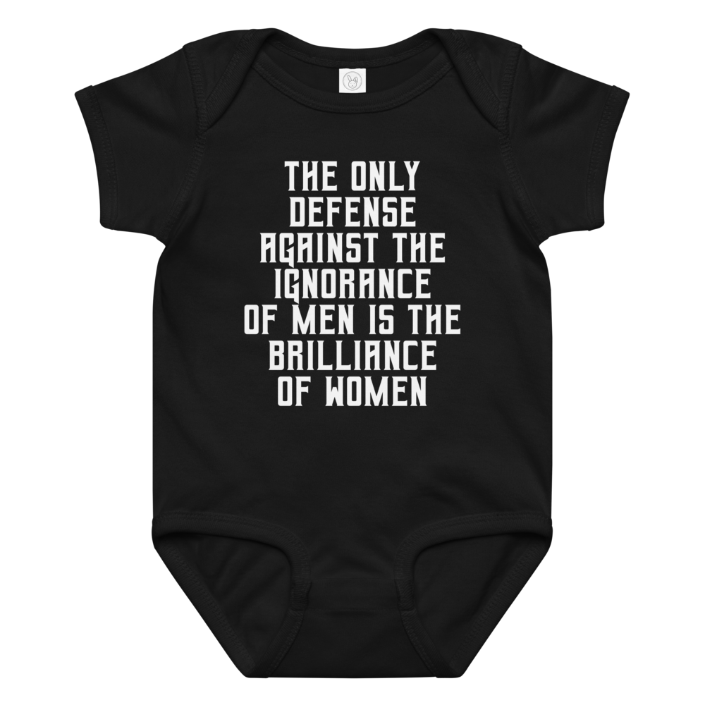 "The Only defense against the ignorance of men is the brilliance of women" printed on a black baby jersey bodysuit laying on a flat surface amongst other clothes