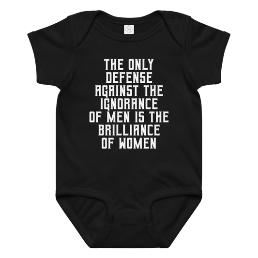 "The Only defense against the ignorance of men is the brilliance of women" printed on a black baby jersey bodysuit laying on a flat surface amongst other clothes