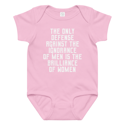 "The Only defense against the ignorance of men is the brilliance of women" printed on a pink baby jersey bodysuit laying on a flat surface amongst other clothes