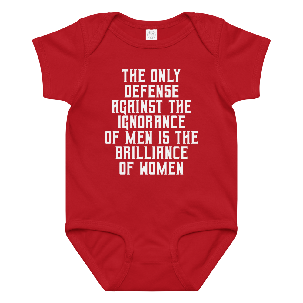 "The Only defense against the ignorance of men is the brilliance of women" printed on a red baby jersey bodysuit laying on a flat surface amongst other clothes
