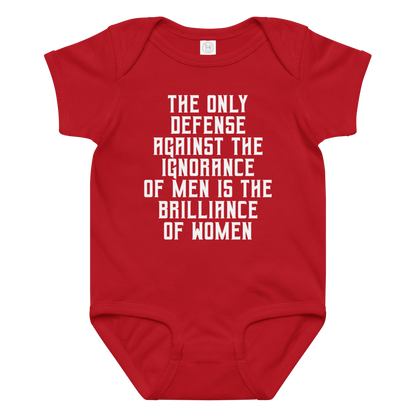 "The Only defense against the ignorance of men is the brilliance of women" printed on a red baby jersey bodysuit laying on a flat surface amongst other clothes