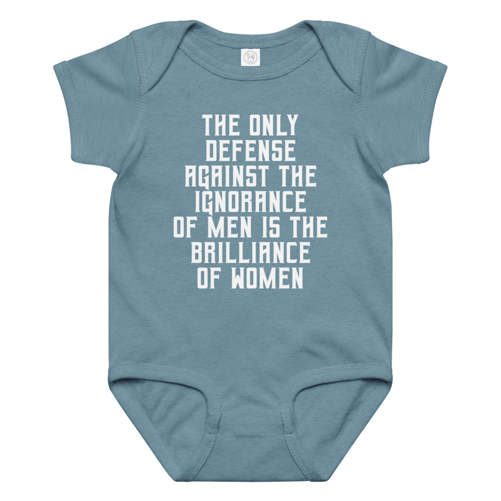 "The Only defense against the ignorance of men is the brilliance of women" printed on a vintage indigo baby jersey bodysuit laying on a flat surface amongst other clothes