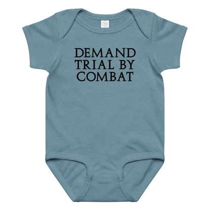 "Demand trial by combat" printed on a vintage indigo baby jersey bodysuit laying on a flat surface amongst other clothes