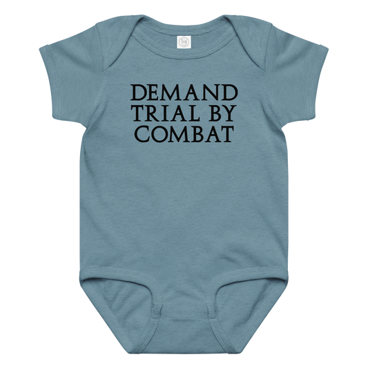 "Demand trial by combat" printed on a vintage indigo baby jersey bodysuit laying on a flat surface amongst other clothes