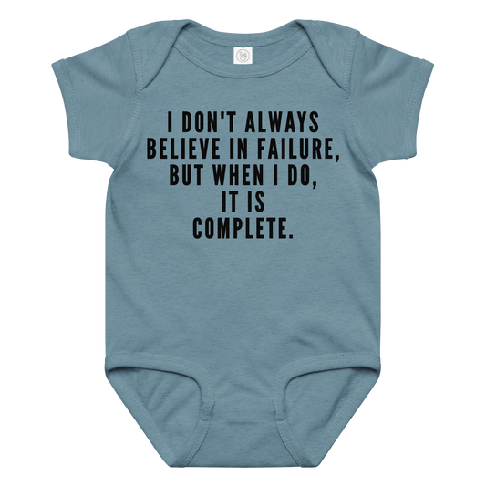 "I don't always believe in failure, but when I do, it is complete." printed on a vintage indigo baby jersey bodysuit laying on a flat surface amongst other clothes