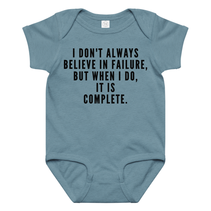 "I don't always believe in failure, but when I do, it is complete." printed on a vintage indigo baby jersey bodysuit laying on a flat surface amongst other clothes