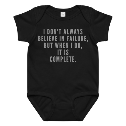 "I don't always believe in failure, but when I do, it is complete." printed on a black baby jersey bodysuit laying on a flat surface amongst other clothes