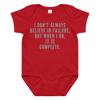 "I don't always believe in failure, but when I do, it is complete." printed on a red baby jersey bodysuit laying on a flat surface amongst other clothes