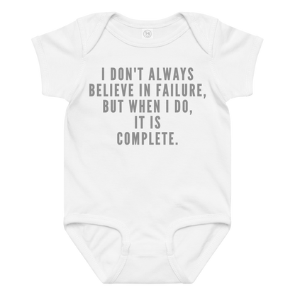 "I don't always believe in failure, but when I do, it is complete." printed on a white baby jersey bodysuit laying on a flat surface amongst other clothes